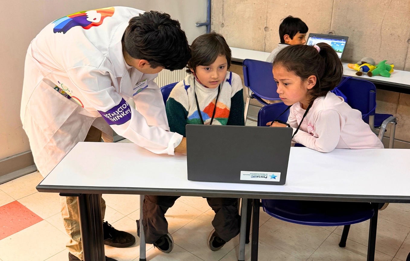 Estudiantes del programa CREA junto a su profesor, trabajando en un computador. Derechos de imagen pertenecen a Penta UC.